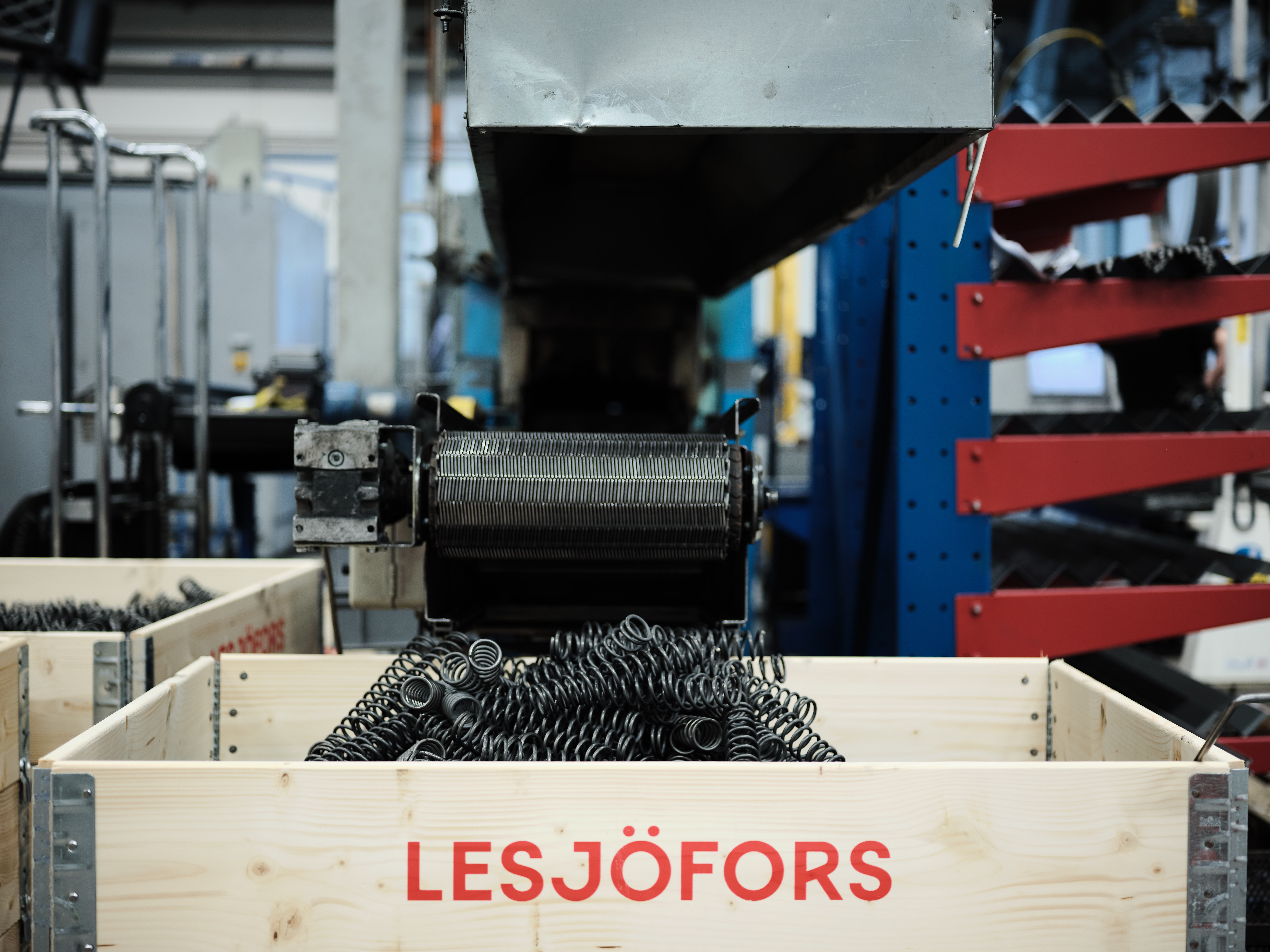 Dark gray metal compression springs falling from a conveyor belt into a wooden crate.