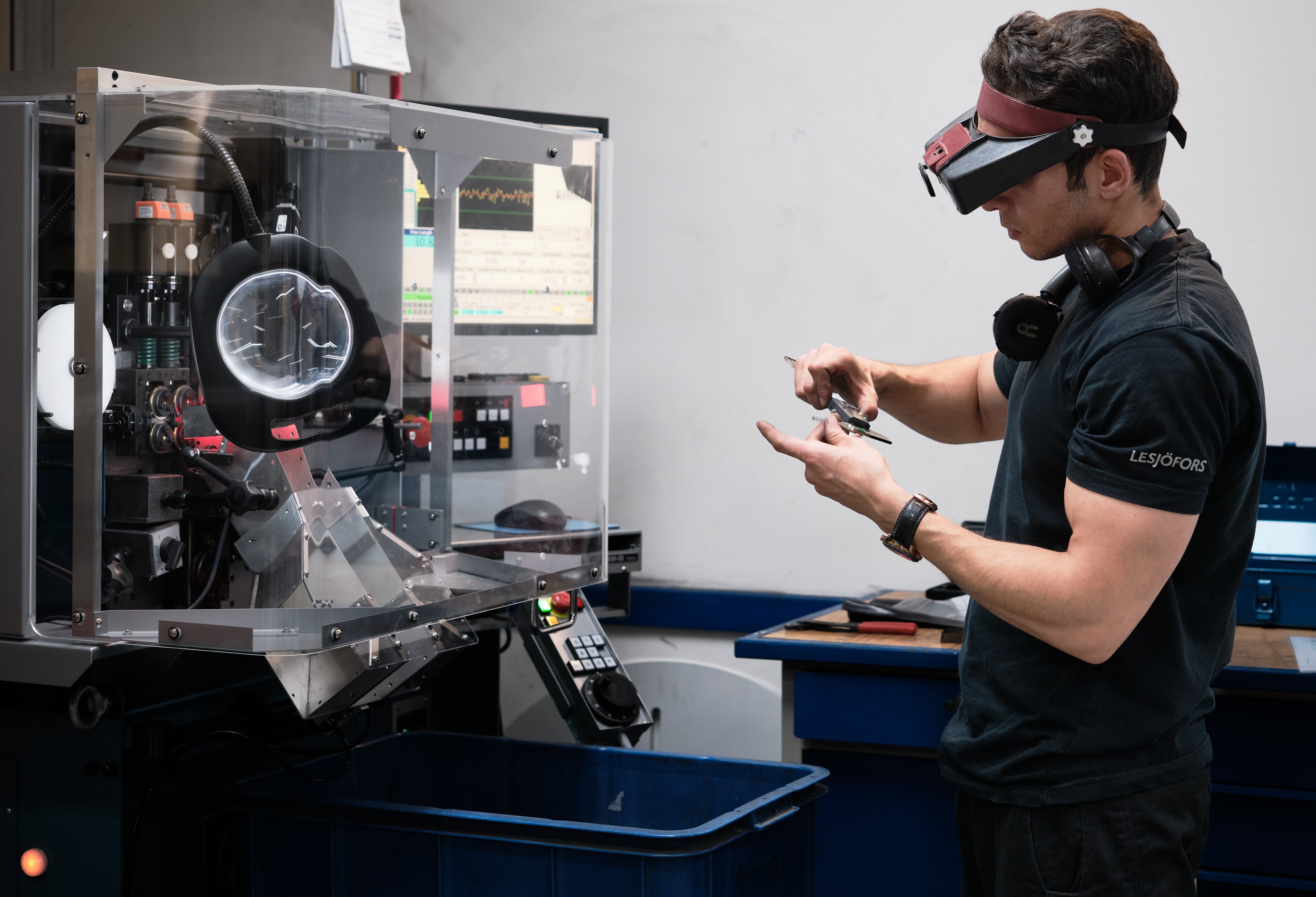 Technician measuring a small metal component beside a CNC coiling machine