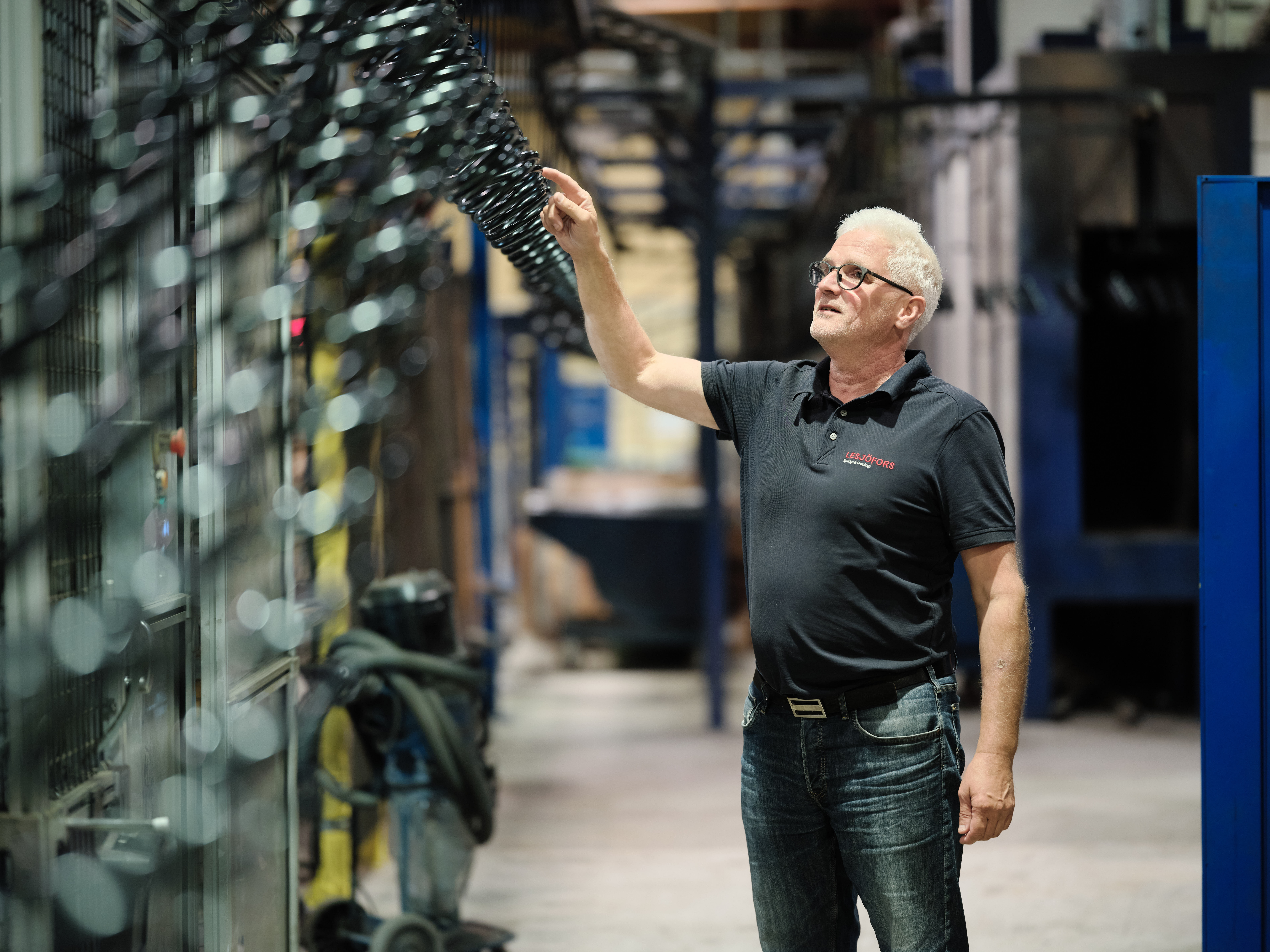 A person in a black shirt examines machinery in an industrial setting, conveying focus and expertise. The environment appears organized and professional.