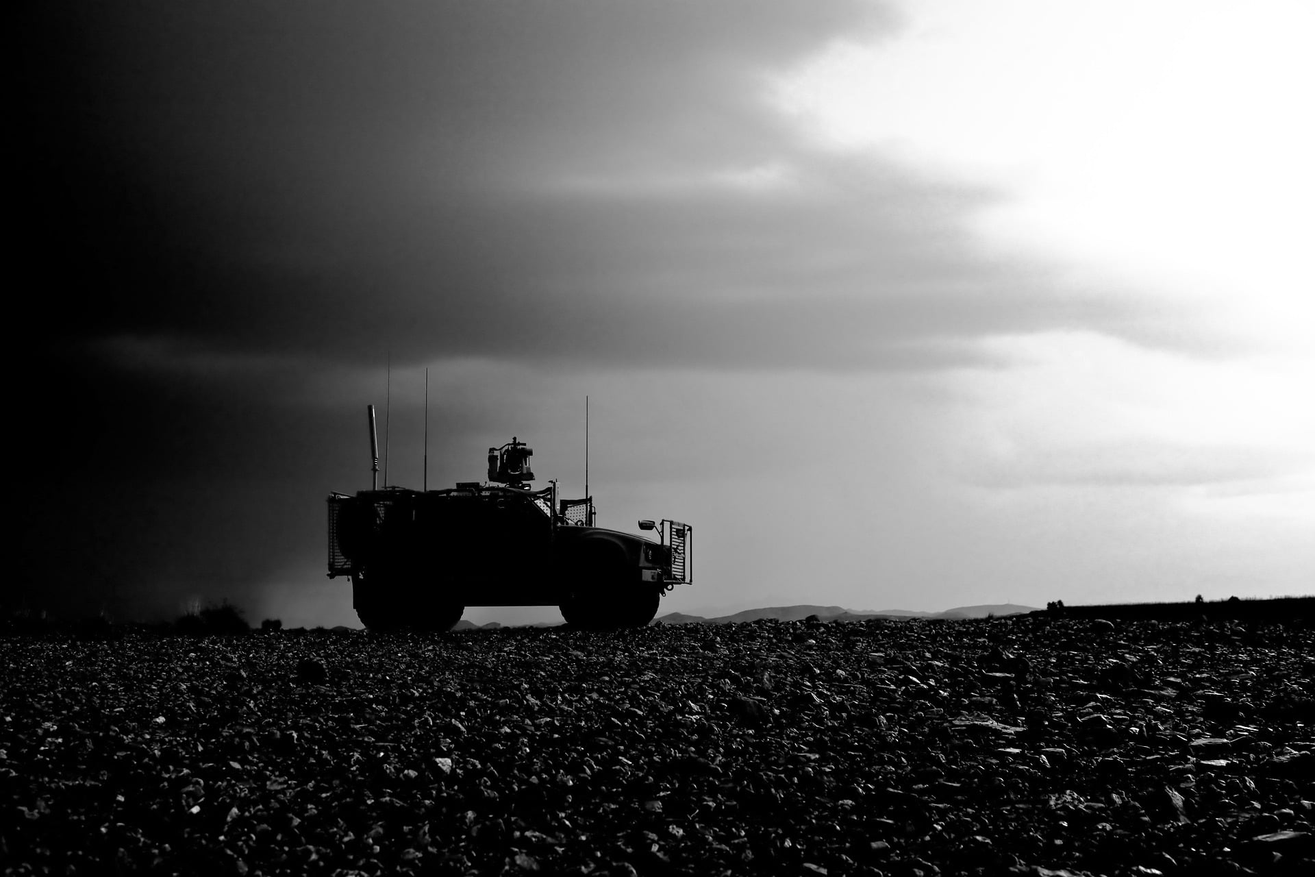 Silhouetted military vehicle on rocky terrain under a dark sky. The contrast of light and dark clouds creates a dramatic view.
