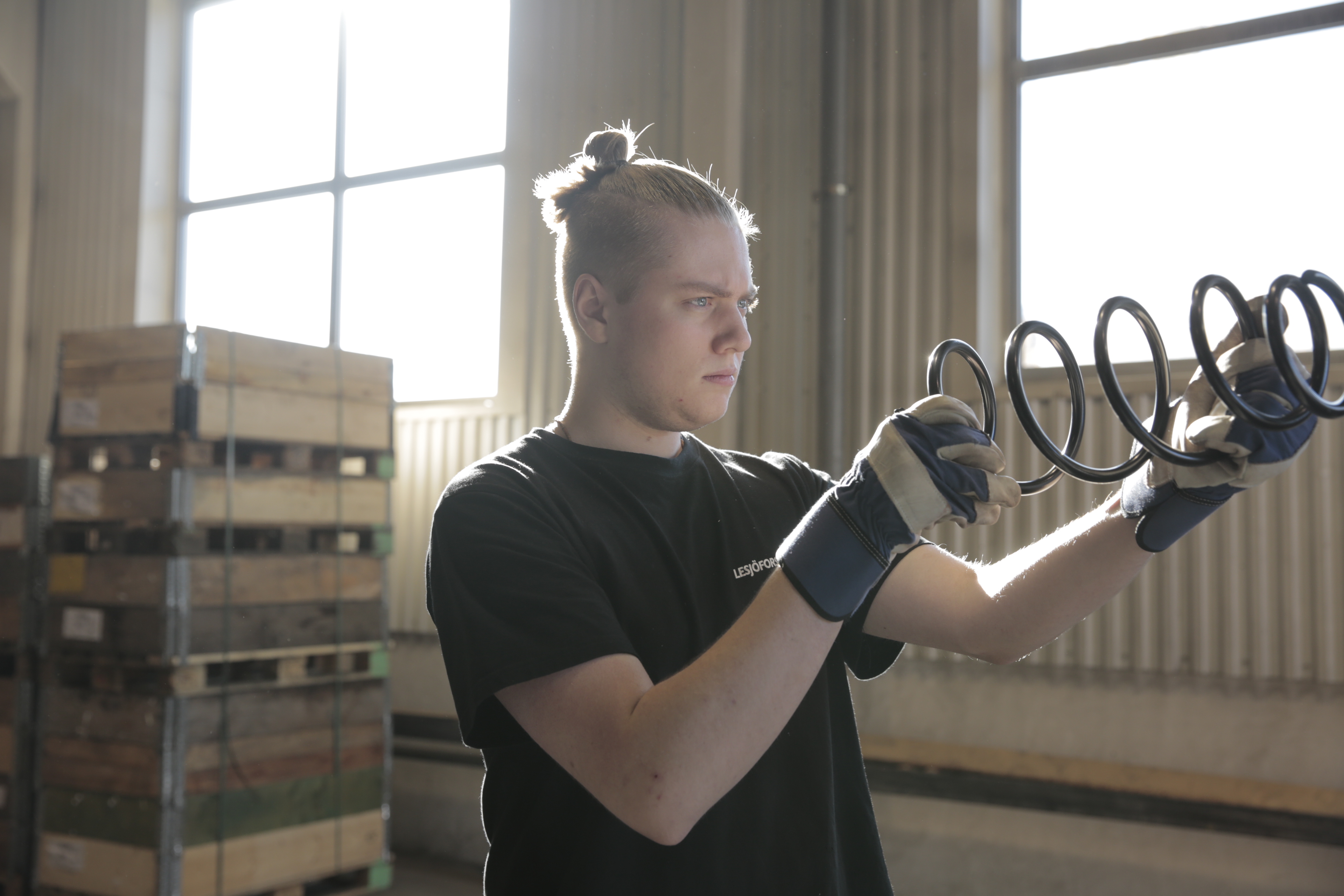 Factory worker inspecting a large coil spring while wearing work gloves.