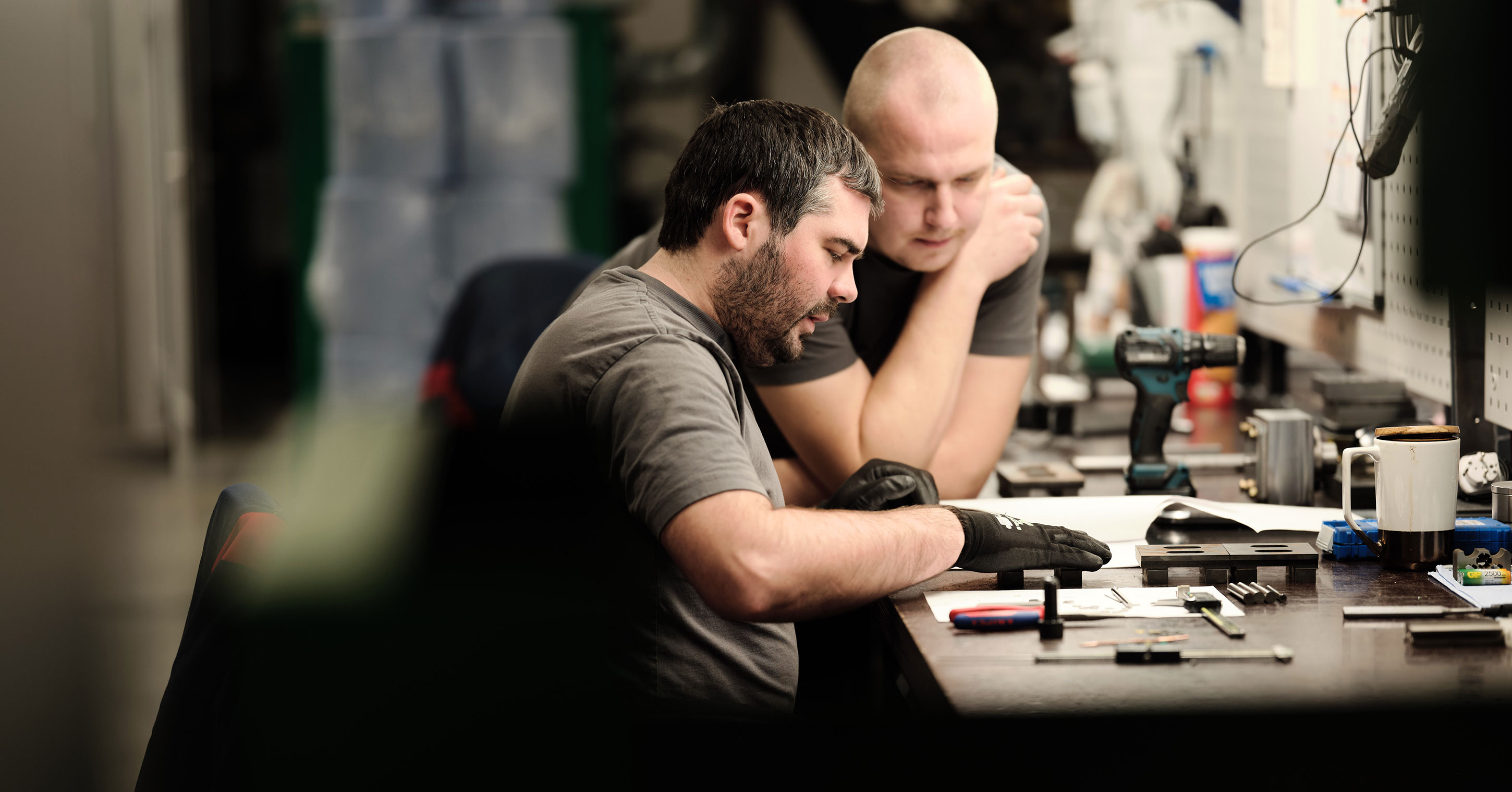 Two coworkers reviewing parts at a workbench in a workshop.