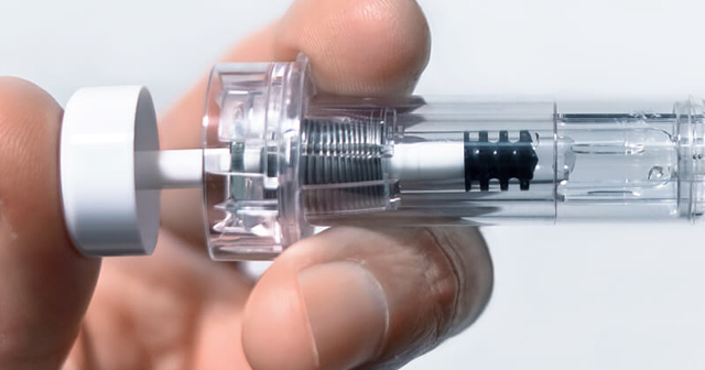 Close-up of a hand holding a transparent syringe with a spring mechanism inside.