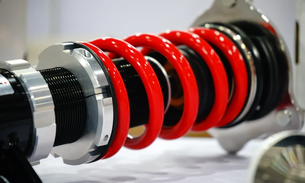 A close-up of a red powder-coated coil spring mounted on a black and silver automotive shock absorber assembly, displayed on a white surface.