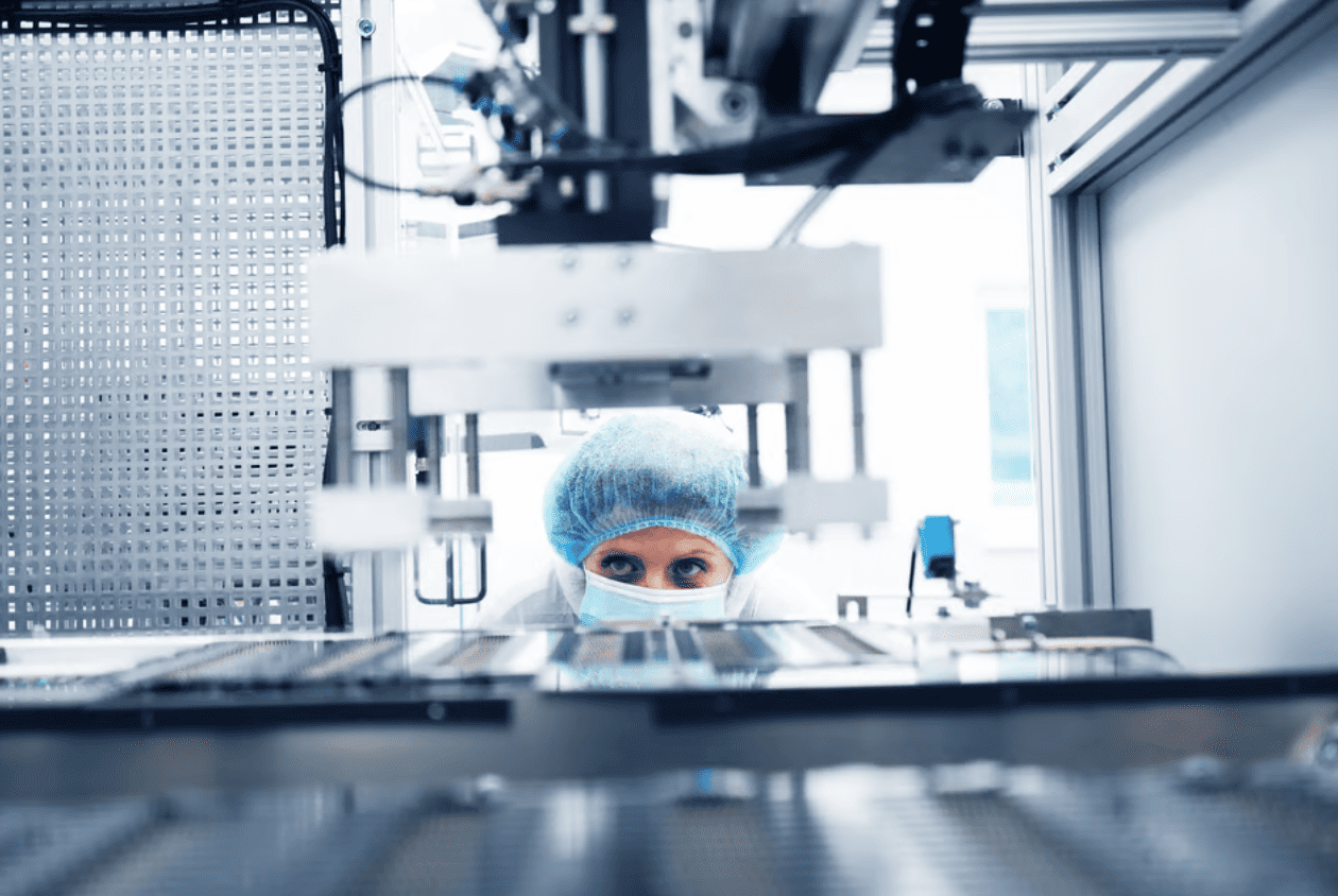 Technician in hairnet and face mask working at a packaging machine in a clean room environment.