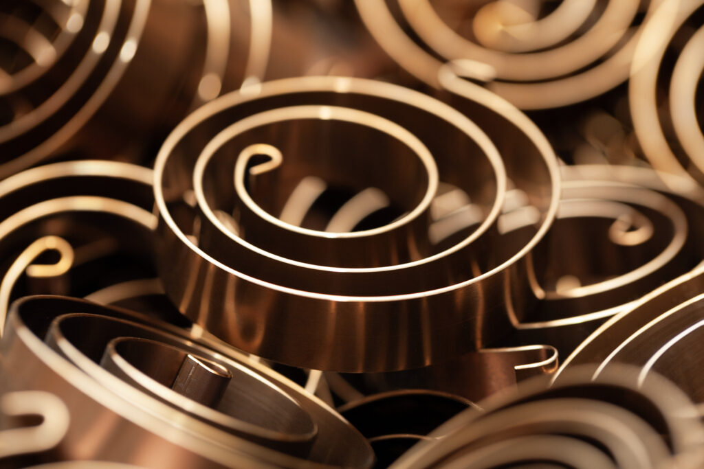Close-up of coiled bronze torsion spiral springs, intricately layered, creating a pattern of circles and spirals. 