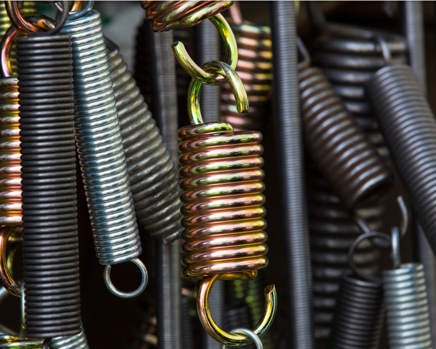 Close-up of assorted metal springs arranged vertically, showcasing varying sizes and colors. The image emphasizes industrial, mechanical textures.
