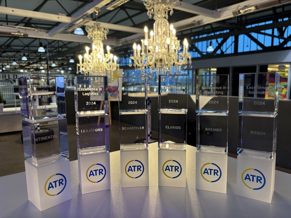 Elegant awards displayed in a row on a white table, with a backdrop of chandeliers and a modern industrial space, creating a sophisticated ambiance.