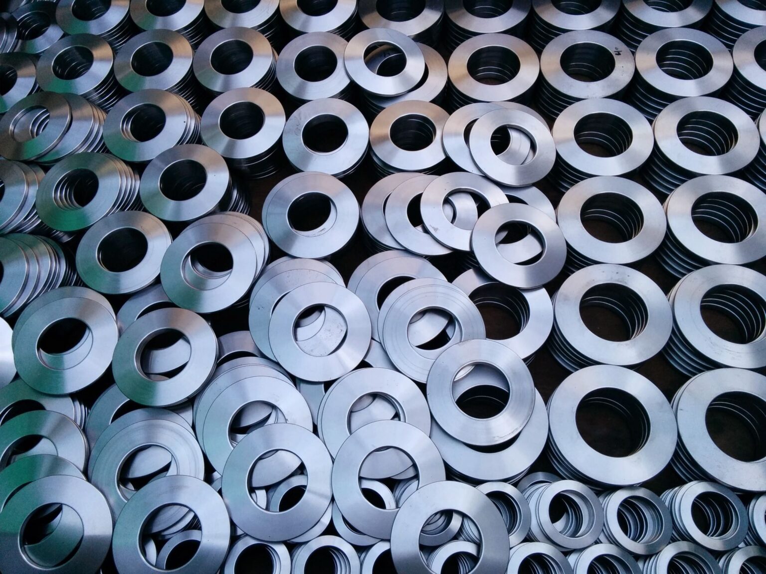 A pile of shiny, metallic sprigs of various sizes, with a circular shape, scattered across a dark surface, creating a textured, industrial pattern.