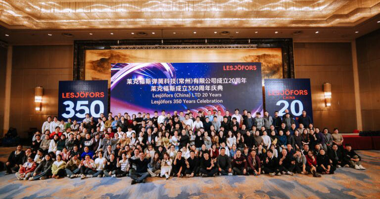 A large group of people posing indoors for a celebratory photo. Behind them, banners read "Lesjöfors 350" and "Lesjöfors (China) LTD 20 Years Celebration."