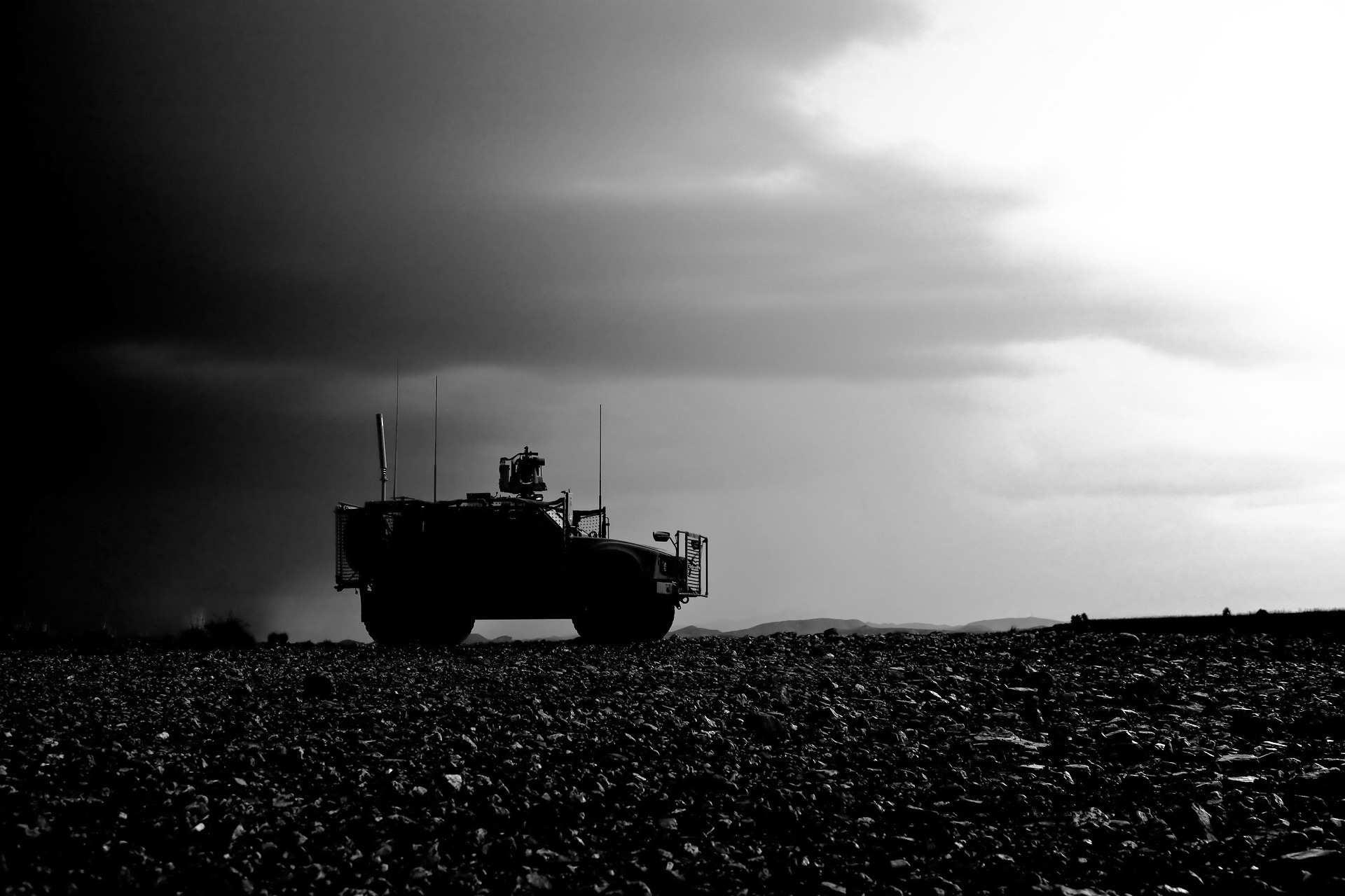 Silhouette of an armored military vehicle on flat, rocky ground under a cloudy sky.