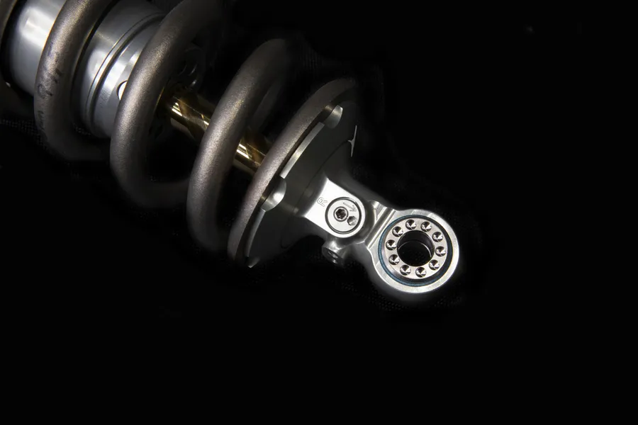 Close-up of a motorcycle suspension shock absorber with coil spring and mounting eyelet.