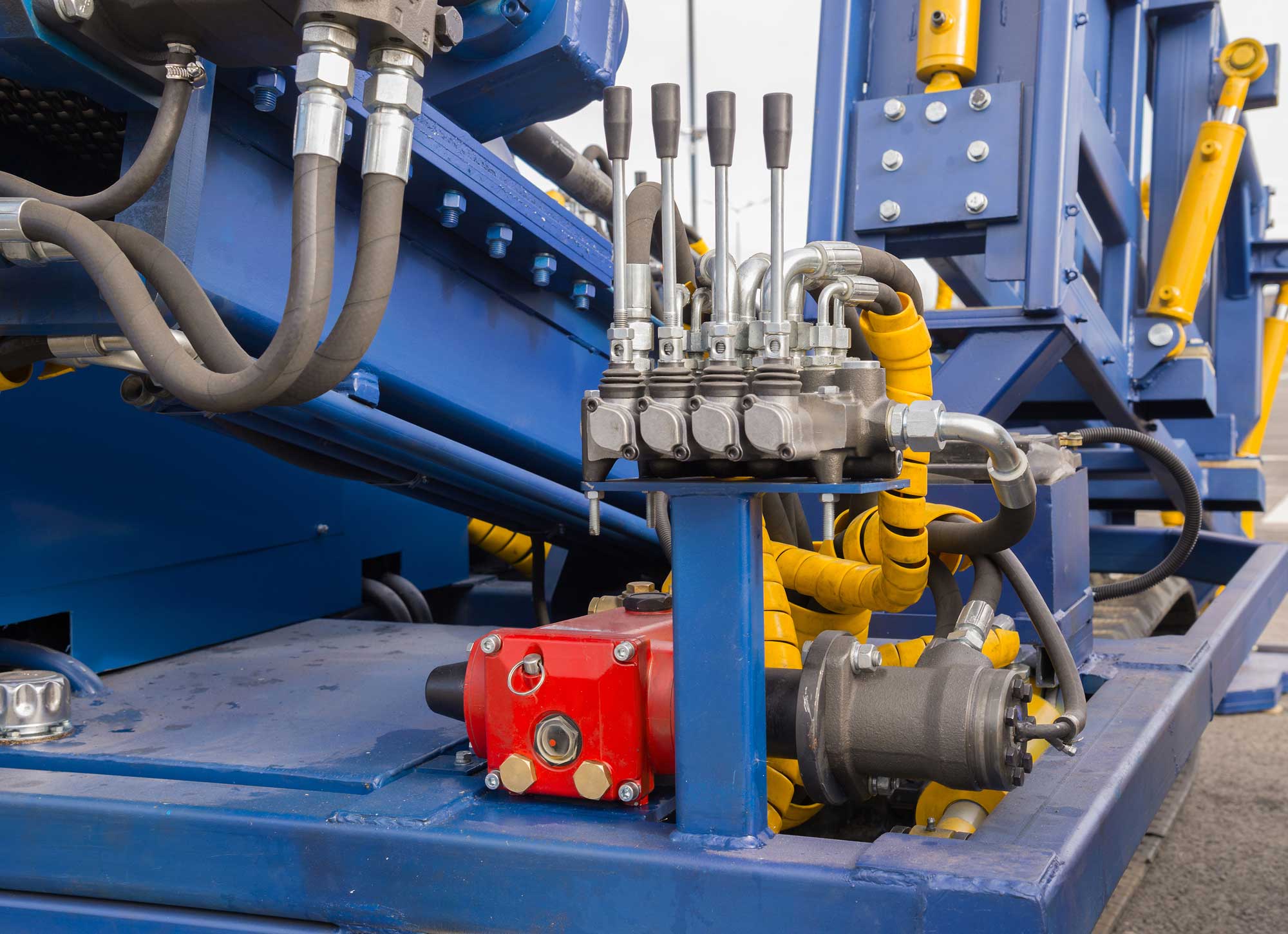 Close-up of industrial hydraulic machinery with blue and yellow components, showcasing valves, tubes, and a red control box.