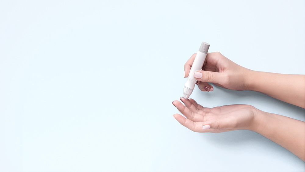 Person using a lancet on their fingertip against a white background, suggesting a blood sugar test.