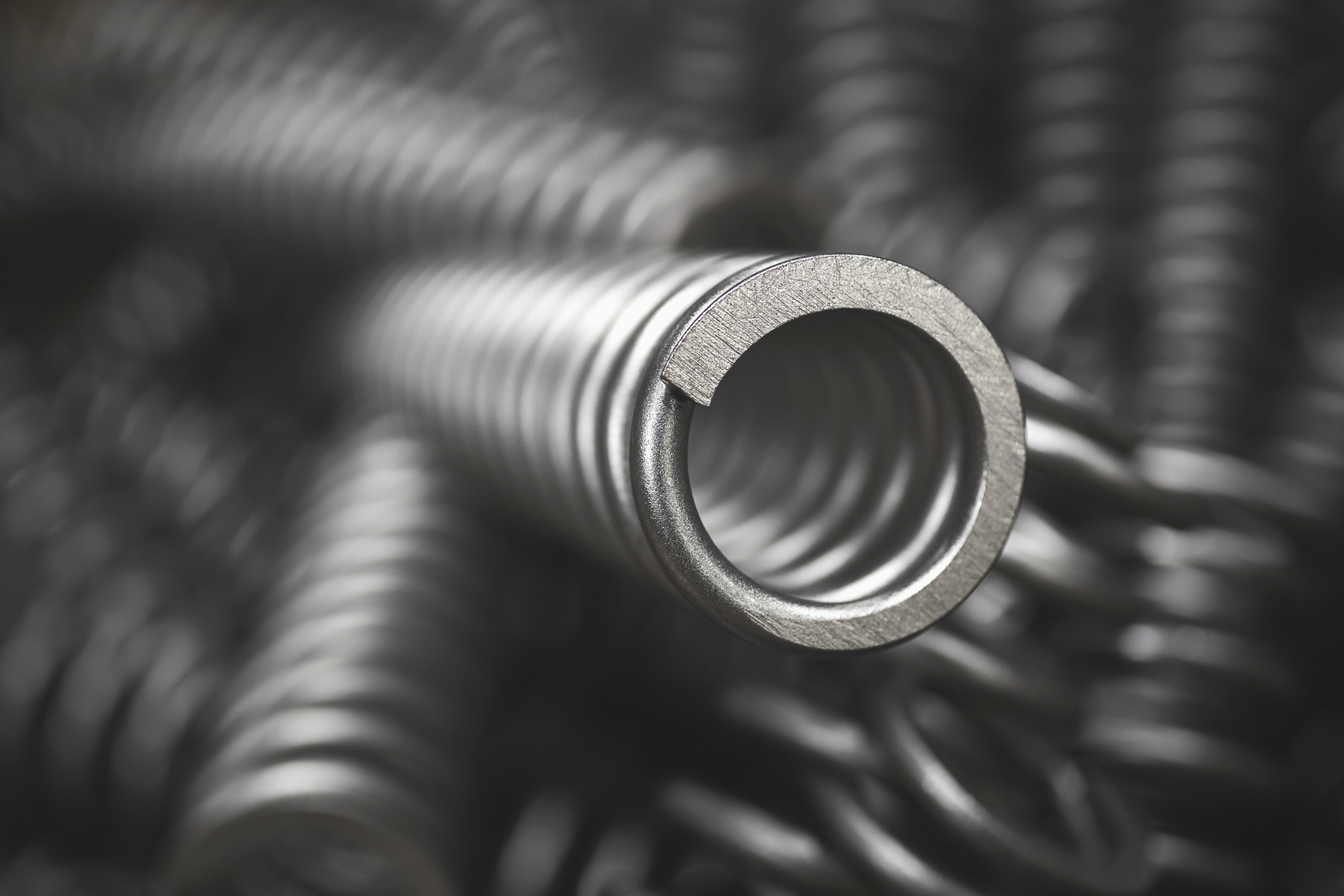Close-up of a shiny metal spring coiled in a spiral pattern. The focus on the spring highlights its smooth texture and precise engineering. The background is blurred.