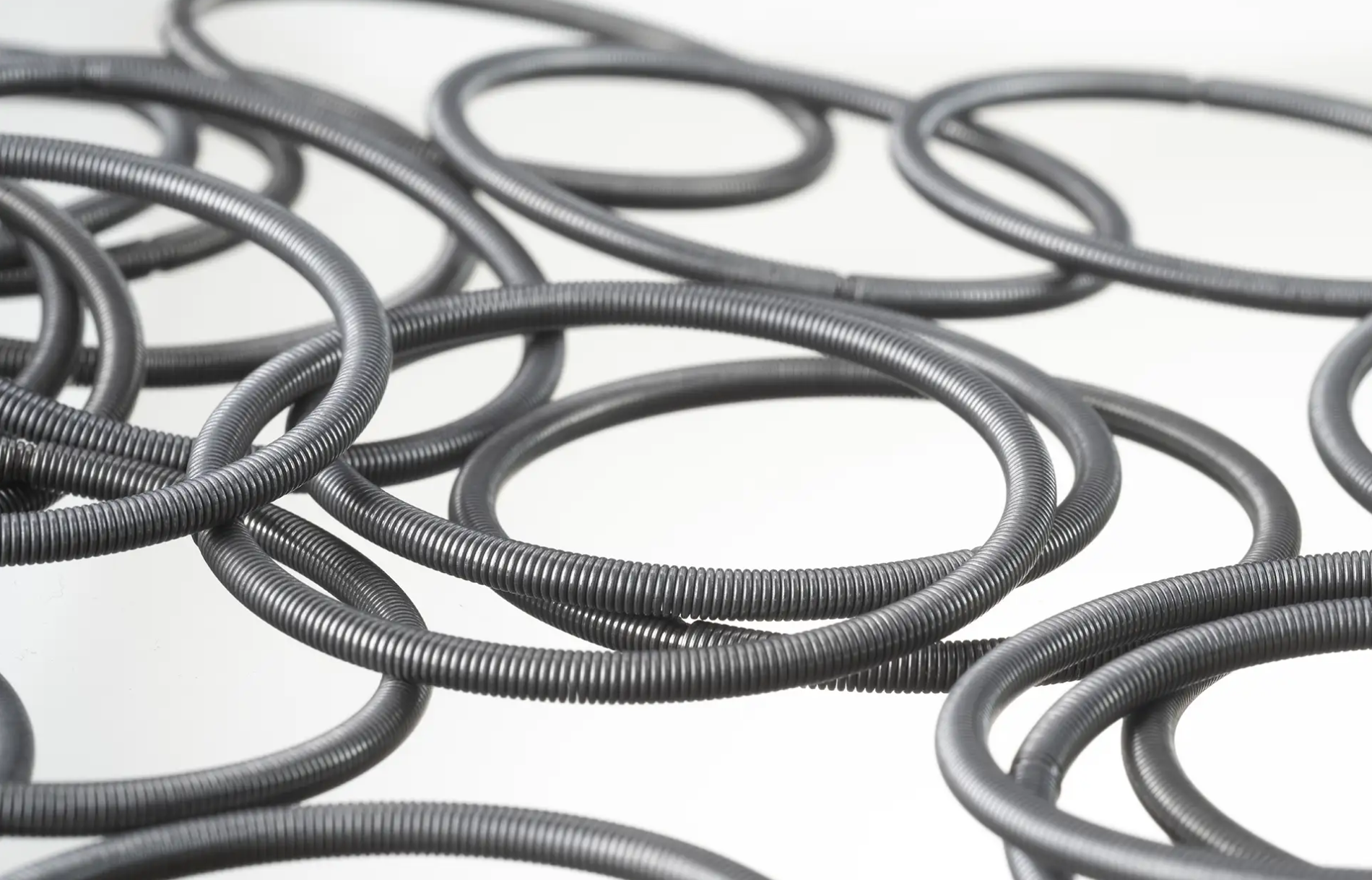 A collection of garter springs scattered on a white surface. The rings vary slightly in size, overlapping each other, creating a textured pattern.