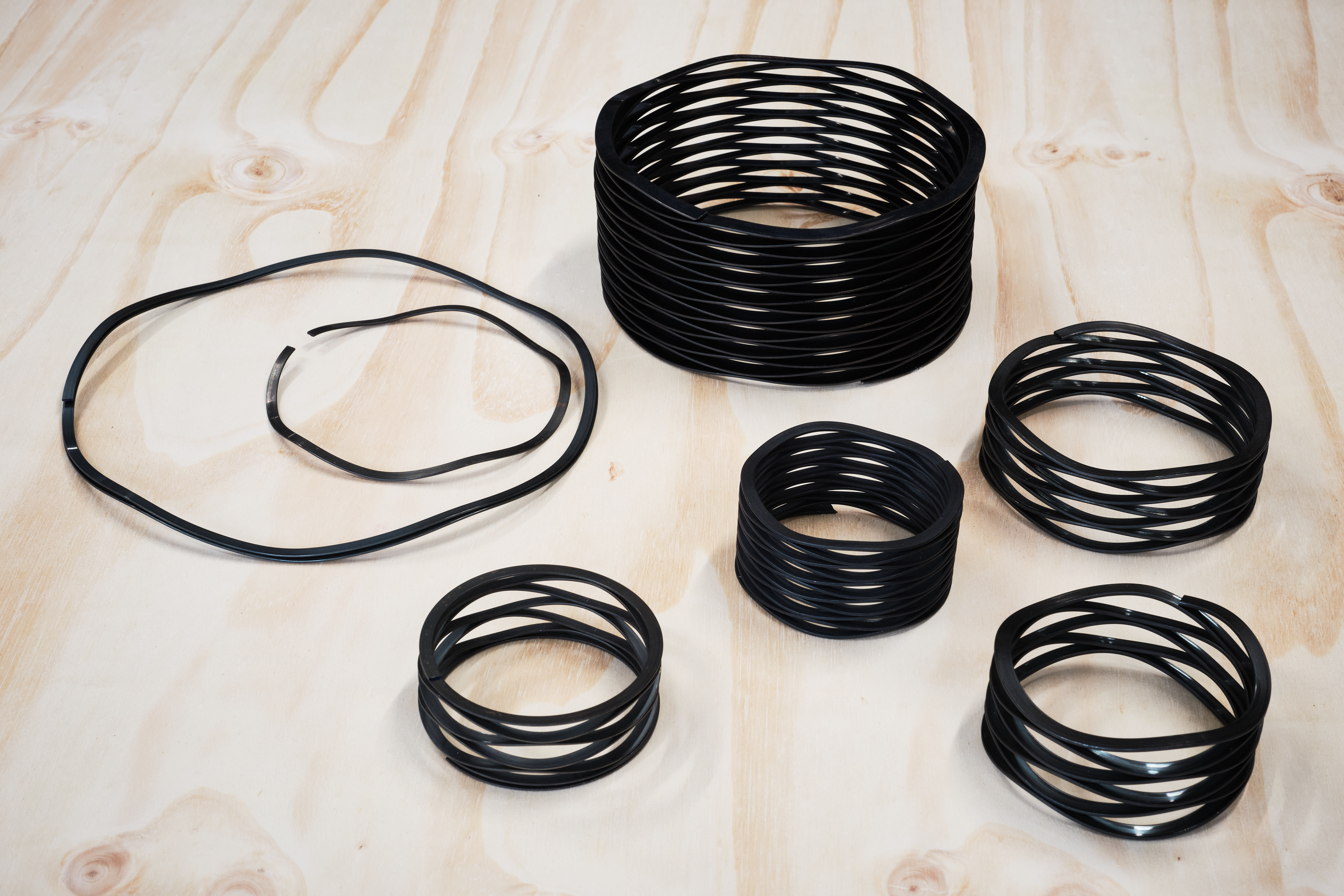A collection of stacked black wave springs of varying sizes, arranged on a light wooden surface.