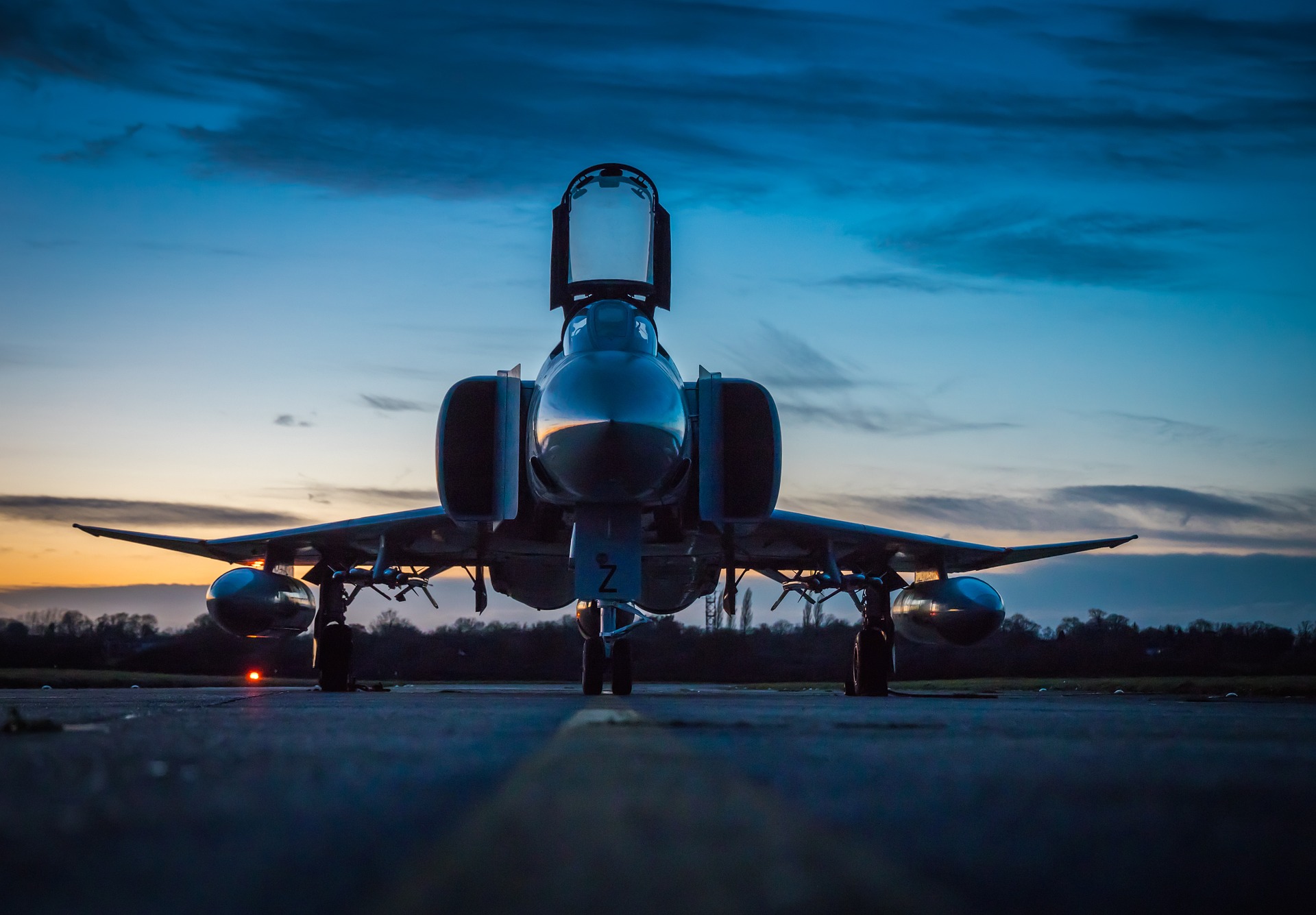 Fighter jet parked on a runway at dusk, silhouetted against a vibrant blue and orange sky, creating a dramatic and powerful atmosphere.