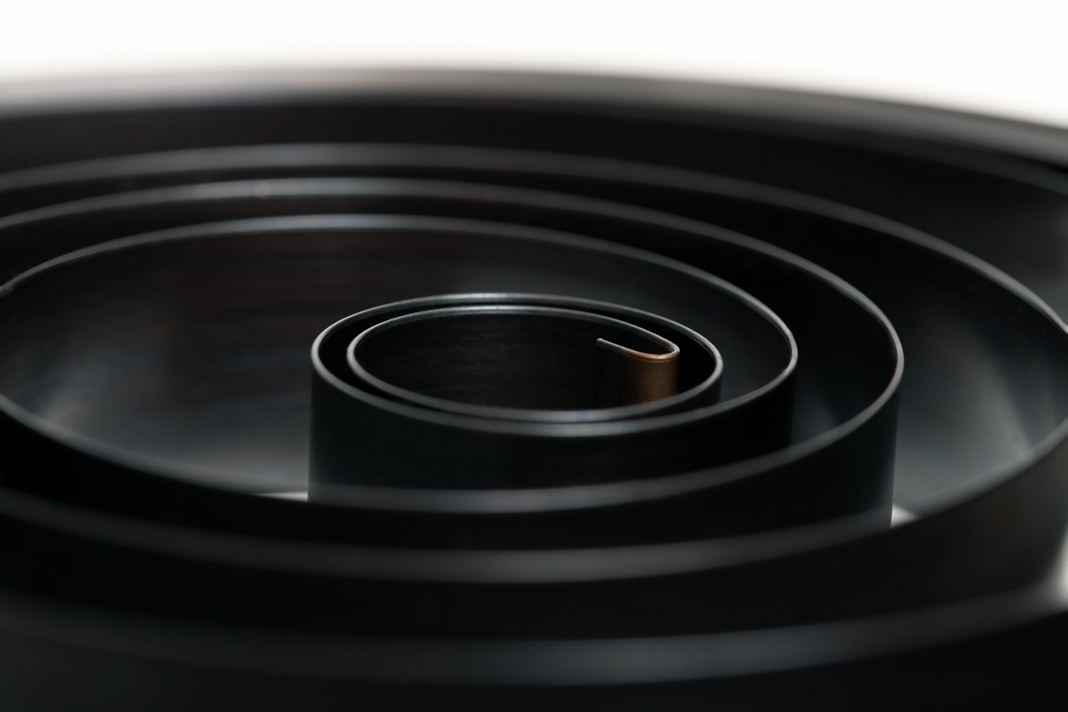 Close-up of a black spiral torsion spring, creating a hypnotic pattern. The glossy surface and circular design convey a sense of motion and precision.