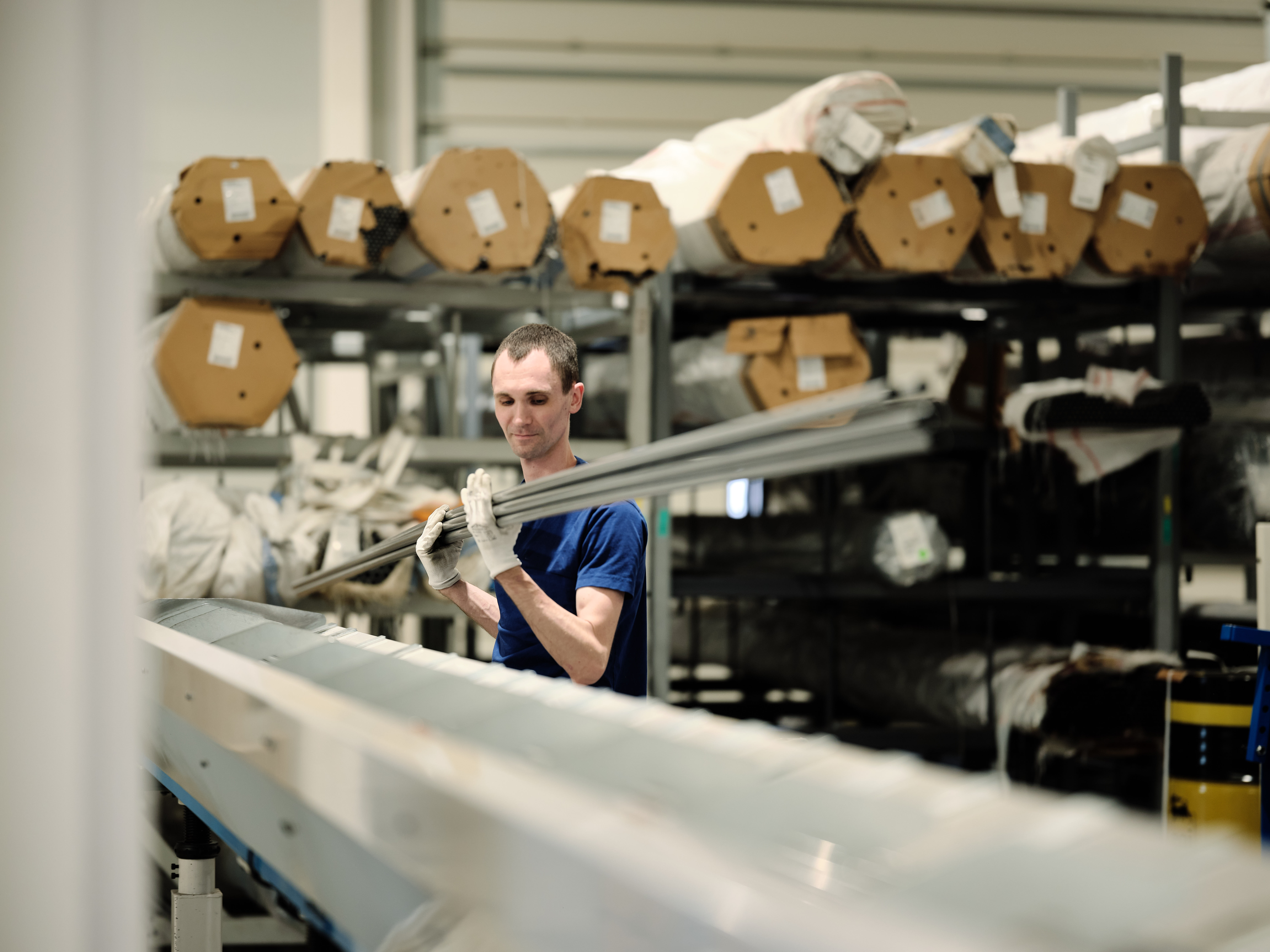 A person in a blue shirt works in an industrial setting, surrounded by shelves of compression gas spring materials.