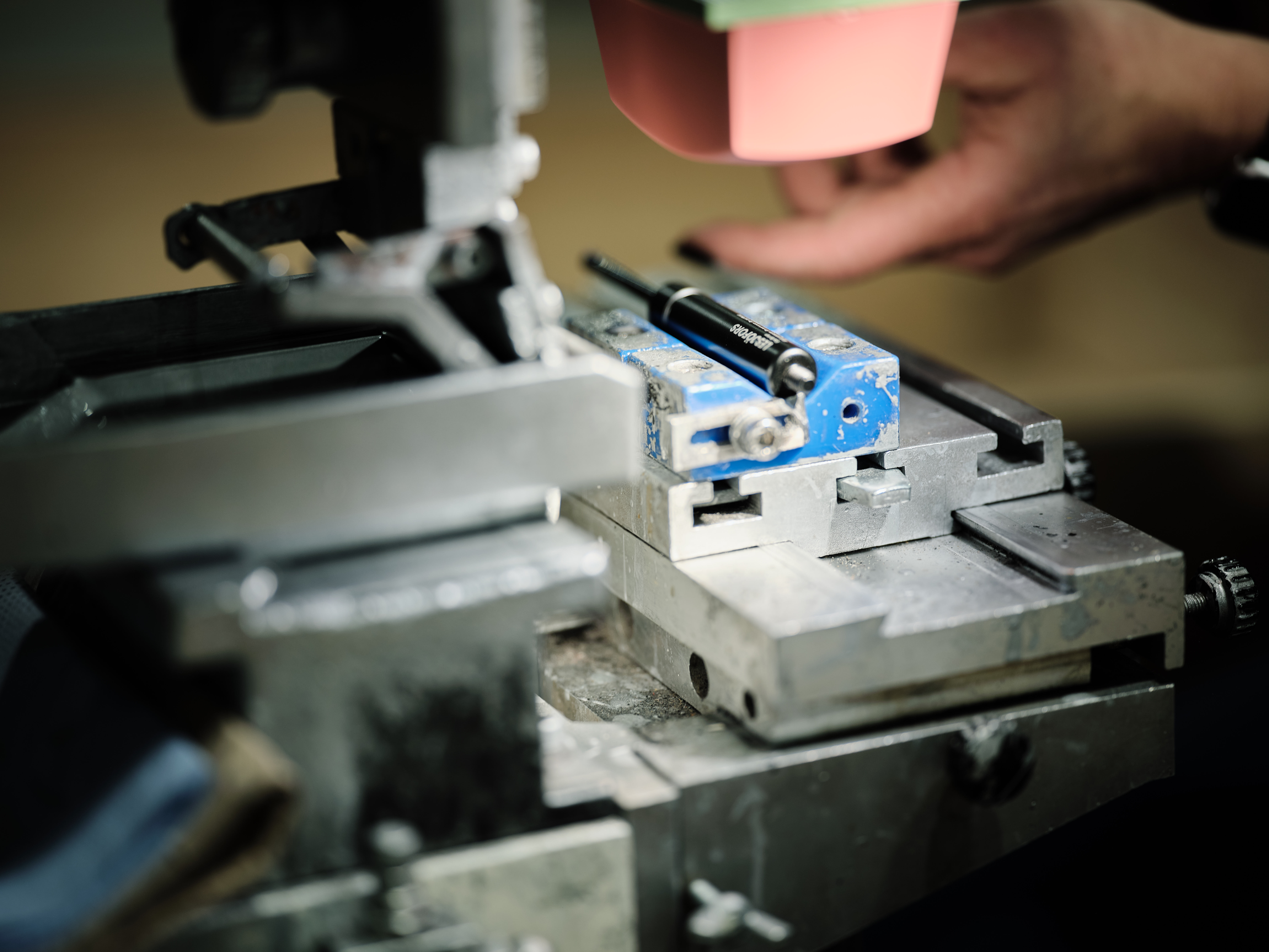 Close-up of a person’s hands producing a spring, guiding a blue component under a tool.